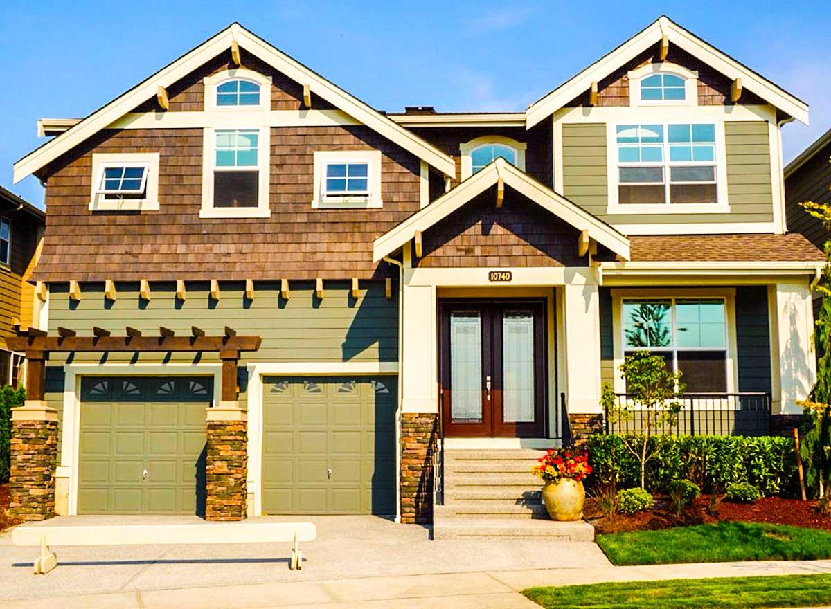 House plan exterior: Two-story home with gables, shingle siding, double garage, arched dormers, and covered entry.