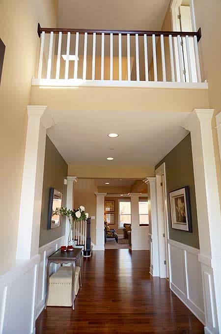 Interior view of foyer with two-story open railing and view into living area. Decorative columns and wainscoting visible.