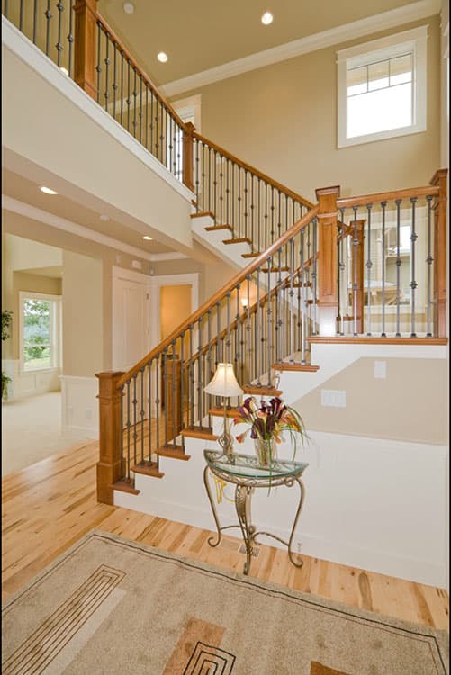 Interior view of a two-story foyer featuring a wooden staircase with ornate metal balusters, a vaulted ceiling, and a window overlooking the exterior.