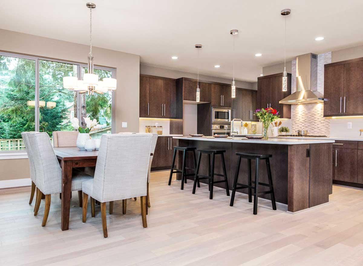 Modern kitchen and dining area with dark wood cabinetry, large island with pendant lights, and dining table with chairs.