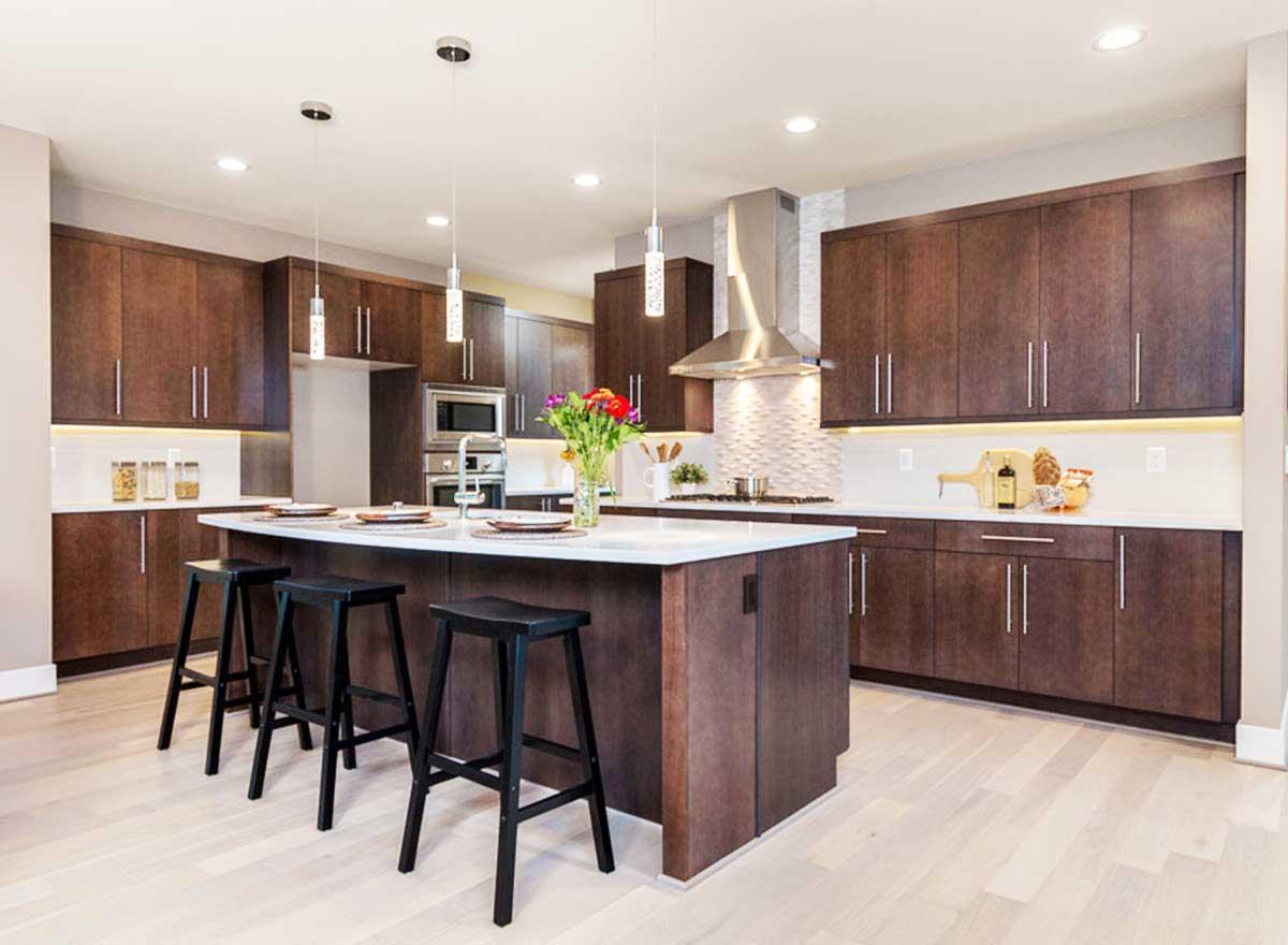 Kitchen interior with dark wood cabinets, central island with seating, stainless steel appliances, and pendant lighting.