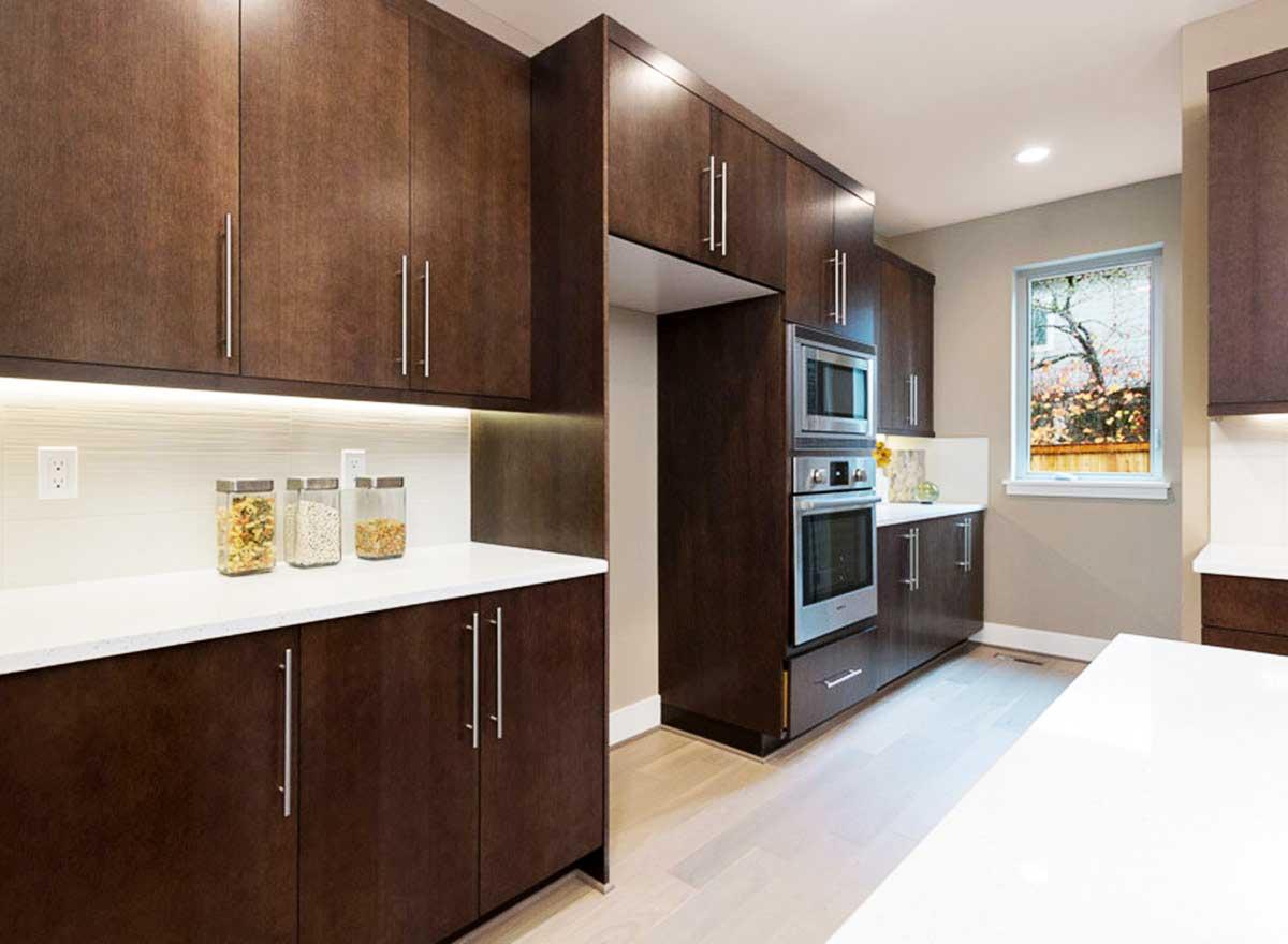 Modern kitchen with dark wood cabinets, white quartz countertops, stainless steel appliances, and under-cabinet lighting.
