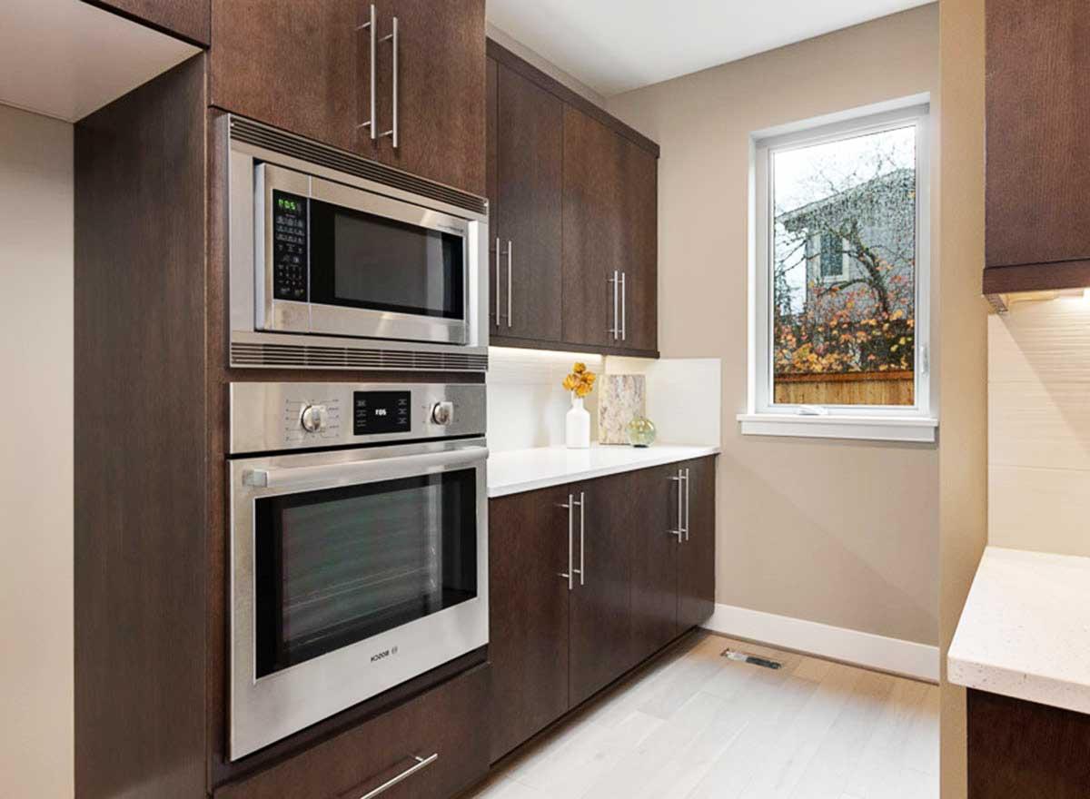 Kitchen with dark wood cabinetry, stainless steel built-in oven and microwave, and a single hung window.