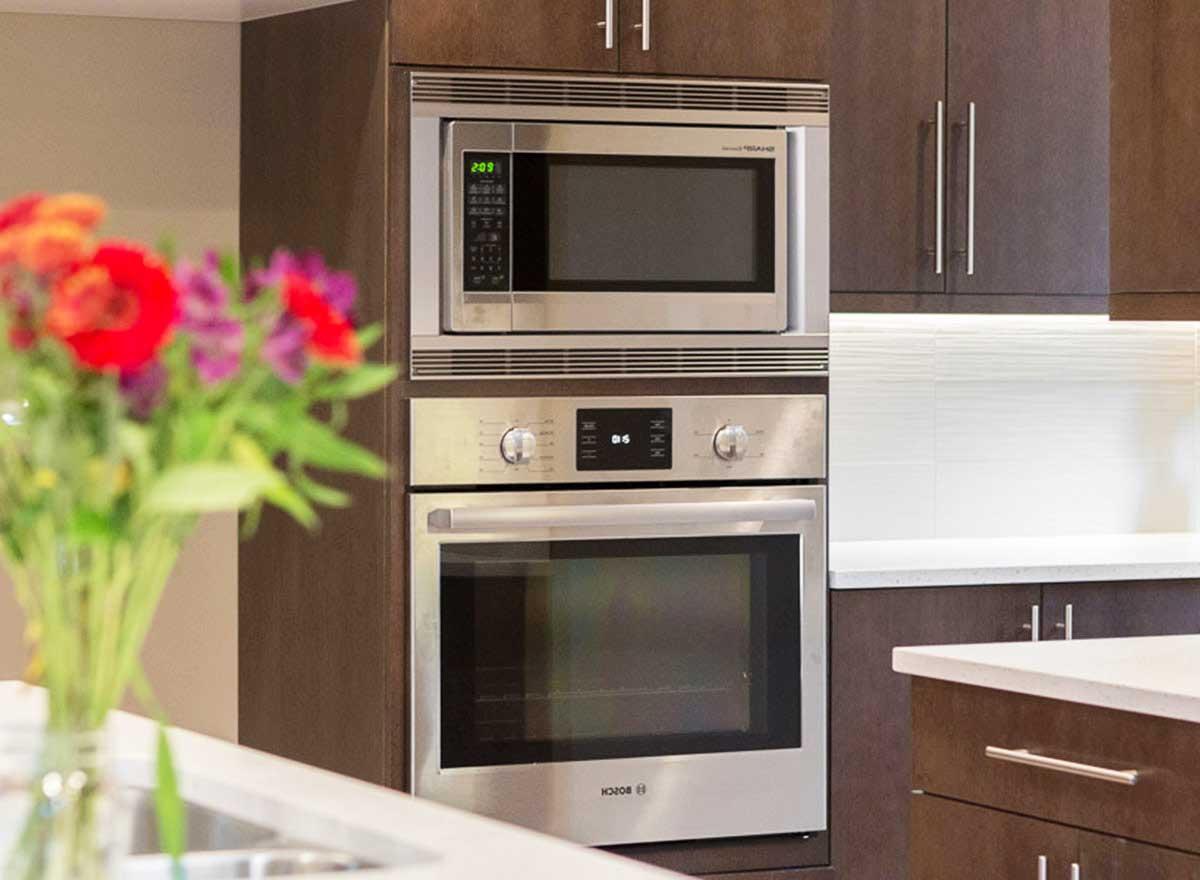 Stainless steel microwave oven stacked above a built-in oven, with dark wood cabinetry.