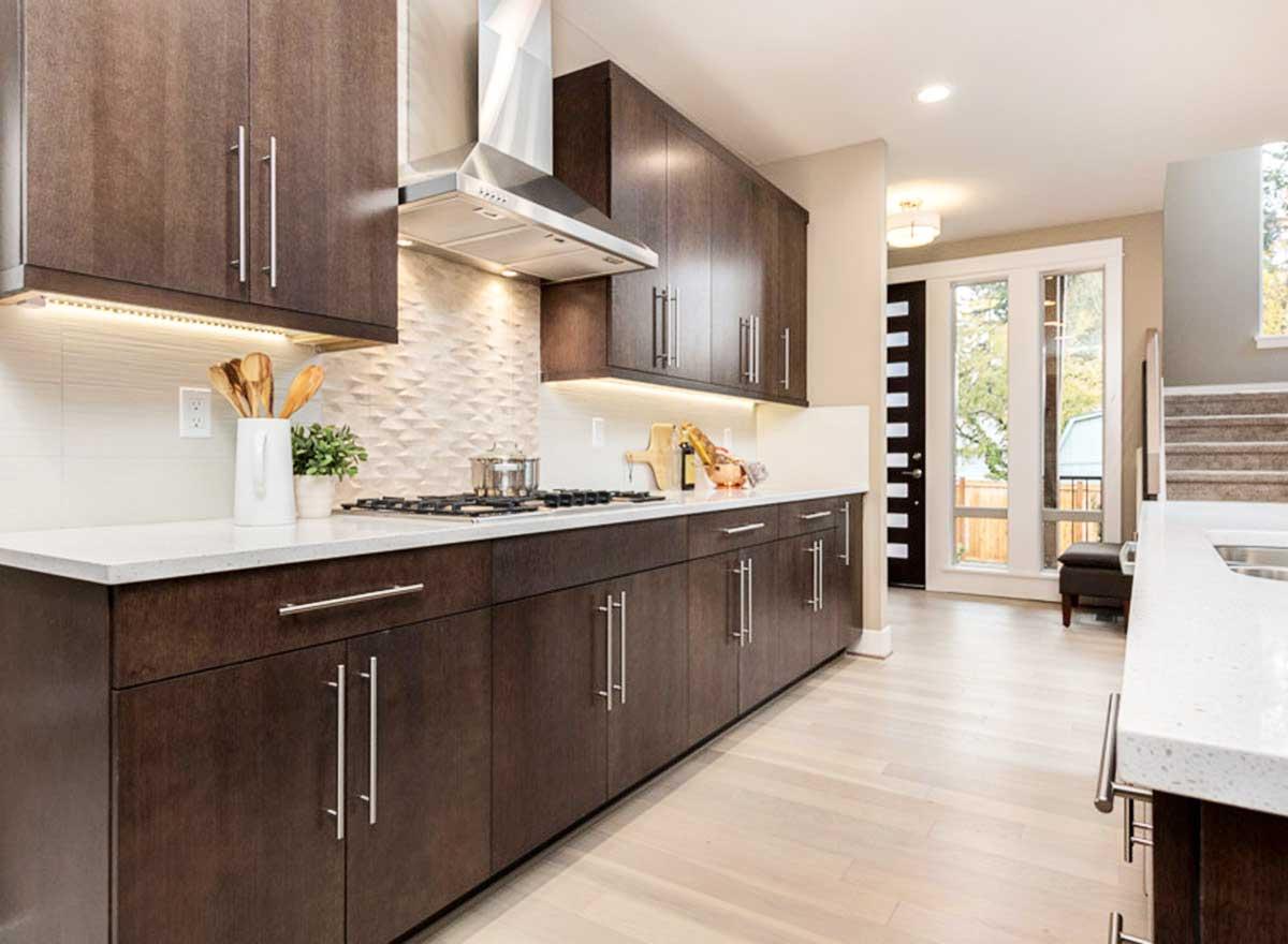 Modern kitchen with dark wood cabinets, white countertops, stainless steel appliances, and textured backsplash.