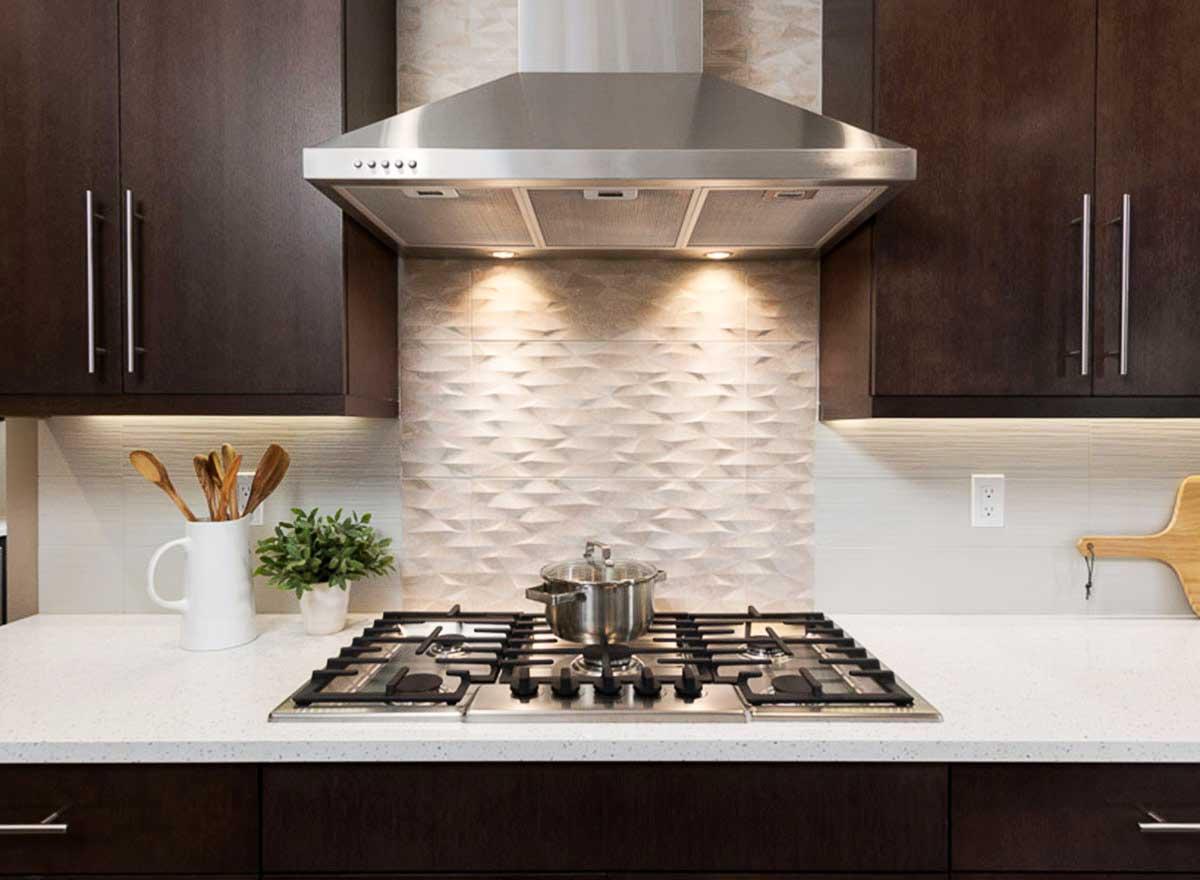 Modern kitchen with dark wood cabinets, stainless steel range hood, and textured tile backsplash.