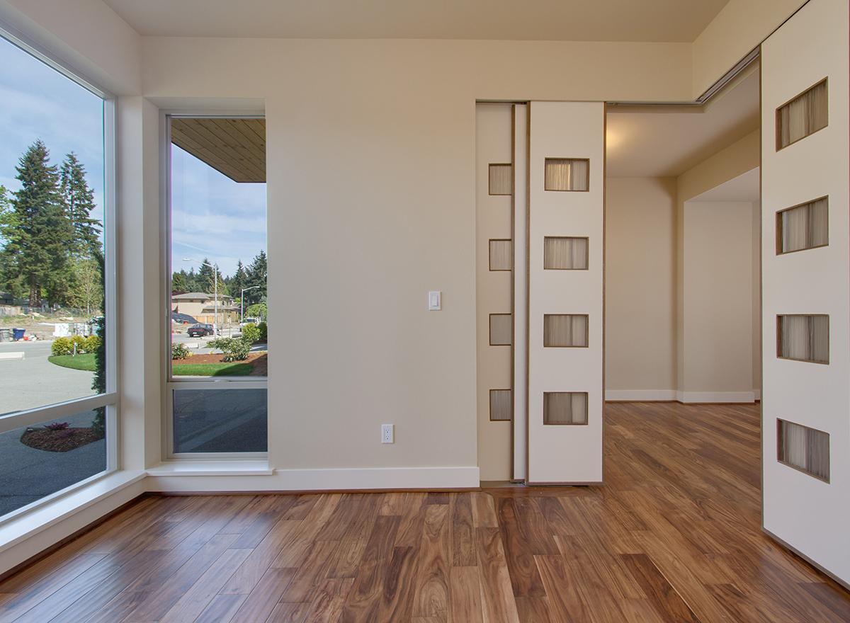 Interior view of a room with corner windows, wood floors, and a sliding panel door with frosted glass inserts.