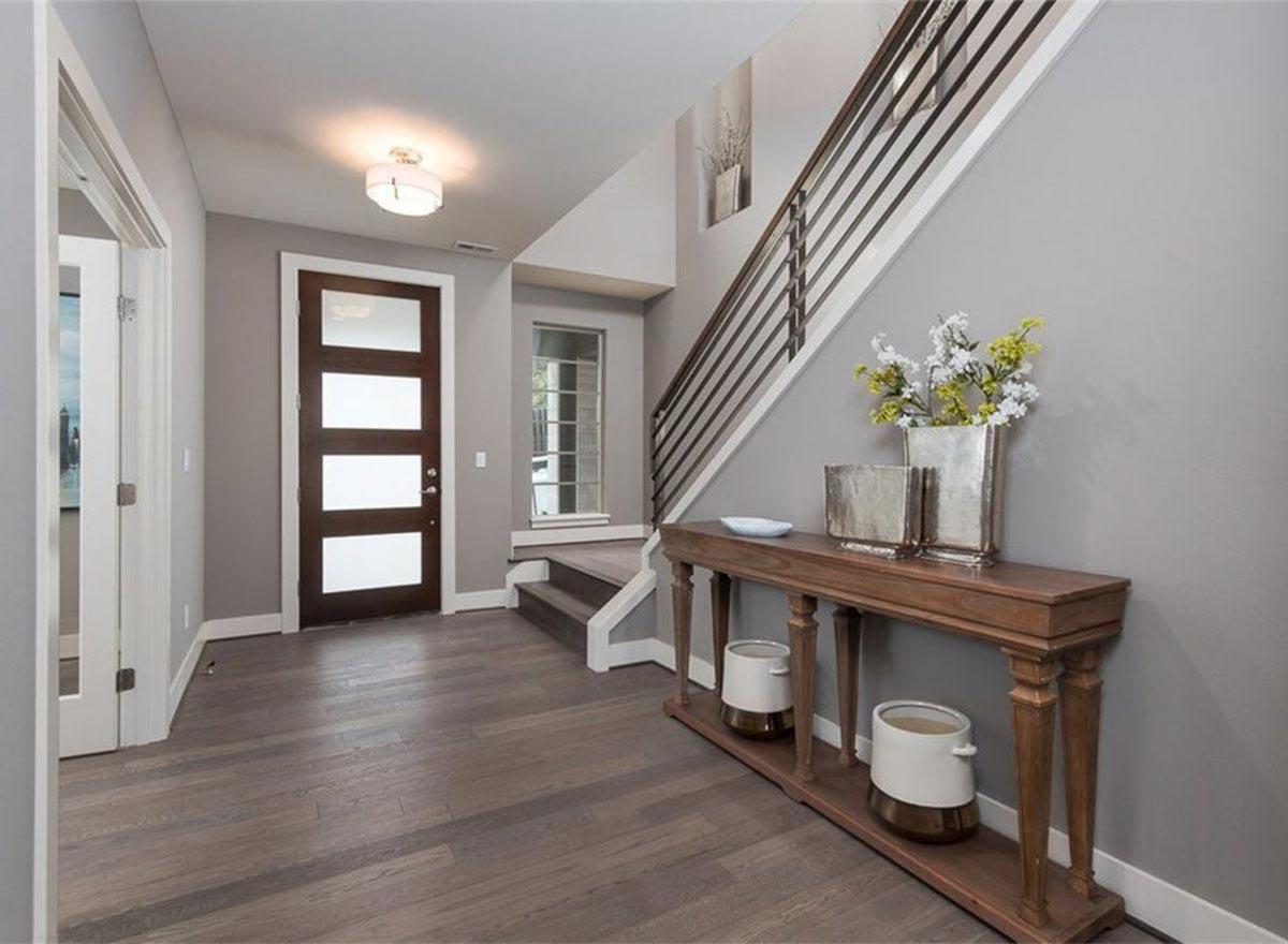 Interior view of modern entryway with dark wood door, glass panels, wood floors, and a sleek staircase with metal railings.