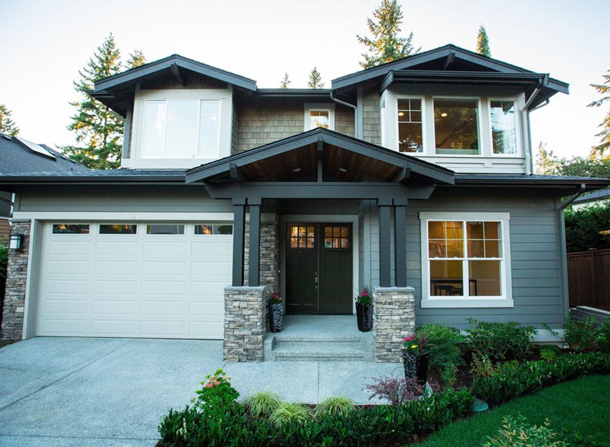 House plan exterior: Two-story home with gabled rooflines, stone-clad porch columns, and a wide garage door.