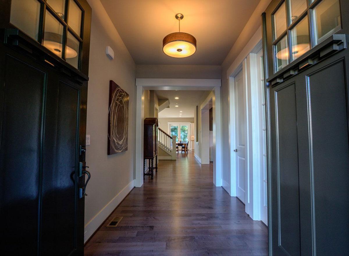 Interior view of a hallway with dark doors, hardwood floors, a staircase, and a view into a dining area.