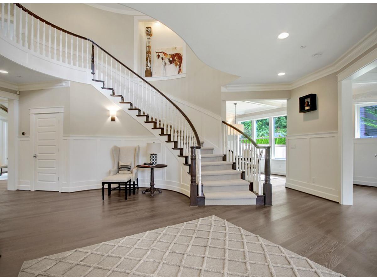 Interior view of grand foyer with curved staircase, white balusters, dark wood handrail, wainscoting, and artwork.