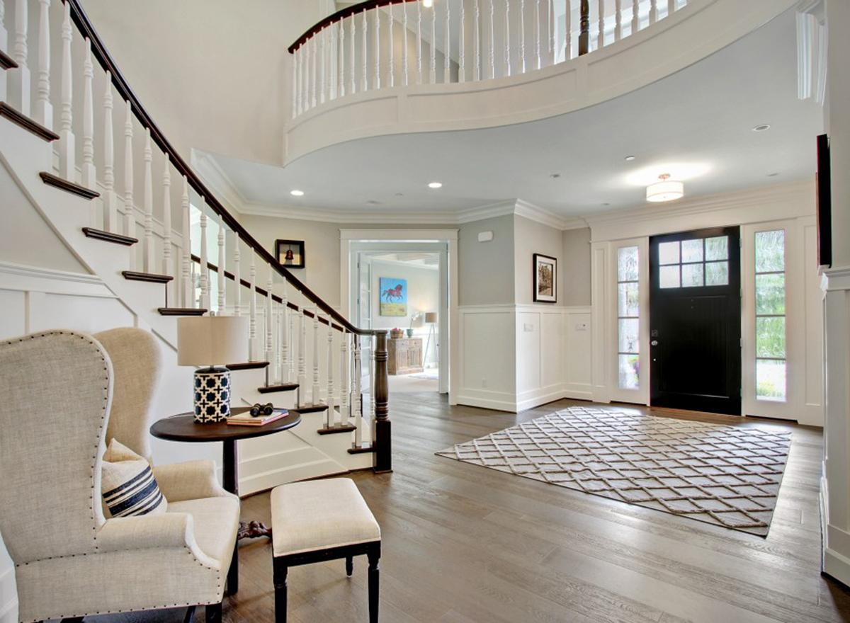 Interior view of house entryway with curved staircase, black front door with sidelights, and wainscoting.