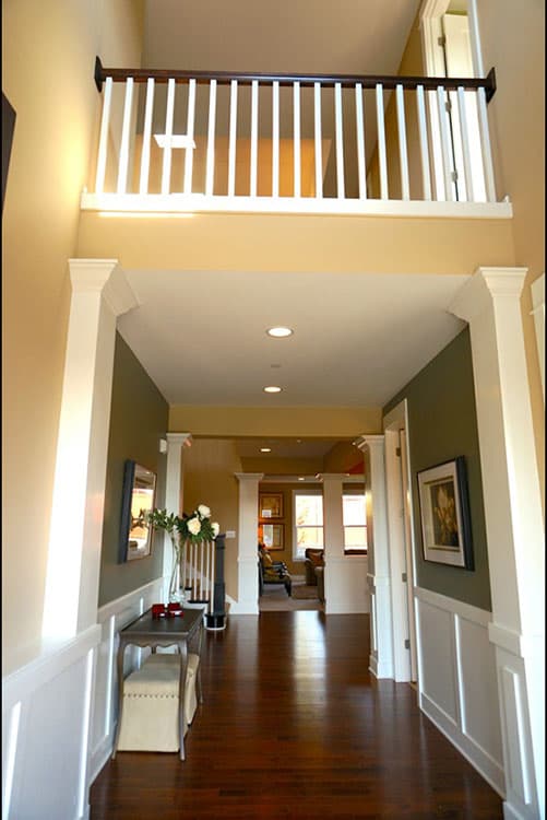 Interior view of a home foyer with a second-story balcony railing, decorative columns, and hardwood flooring.