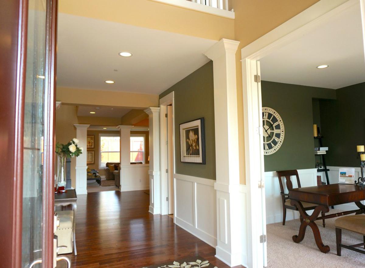 Interior view of a house entry hall with wood floors, pillars, and a view into a living area and study.