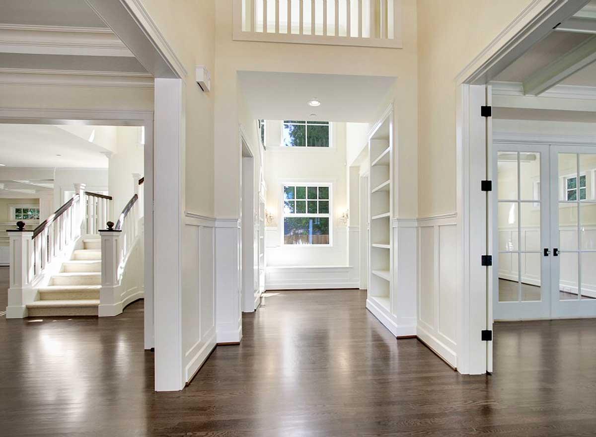 Interior view of hallway with a curved staircase, wainscoting, built-in bookshelves, and double glass doors.