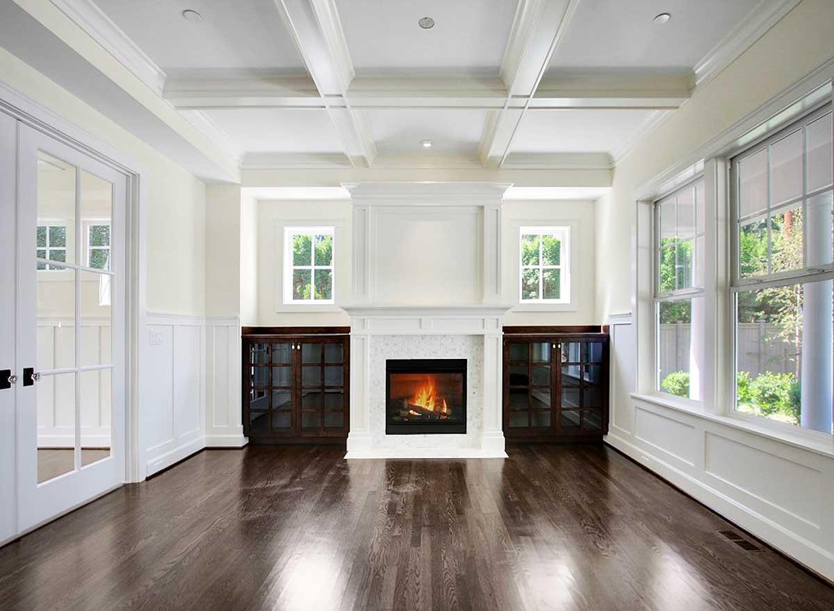 Interior view of living room with coffered ceiling, fireplace, built-in cabinets, and large windows.