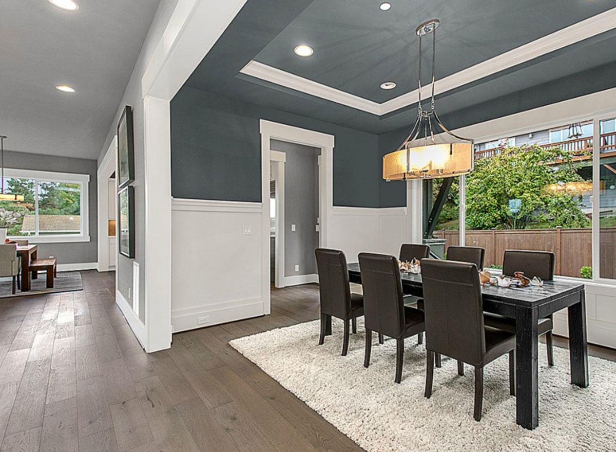 Dining room with a tray ceiling, wainscoting, dark wood table with chairs, and large windows overlooking a backyard.