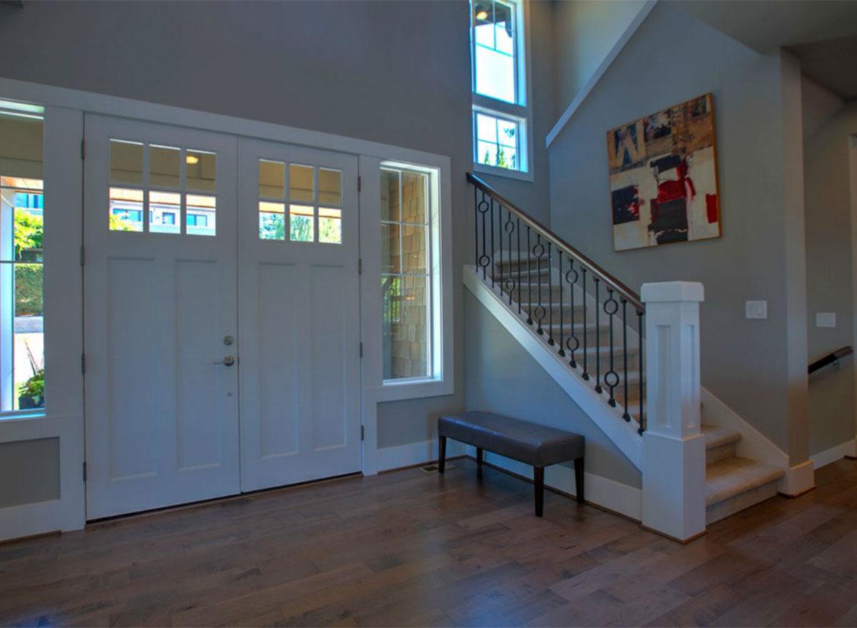 Foyer with double entry doors, large windows, and a carpeted staircase with decorative metal railings.