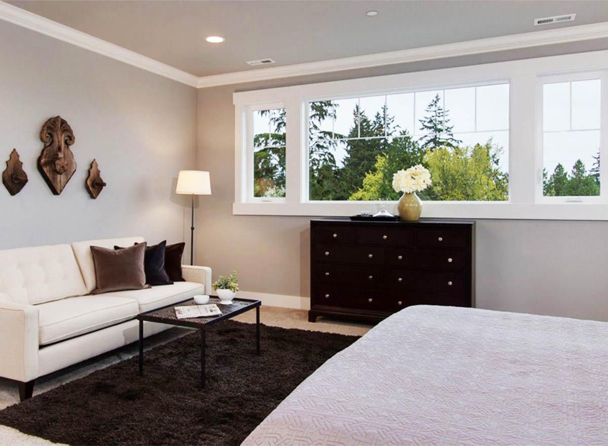 Bedroom with white sofa, dark dresser, and large picture window overlooking trees.