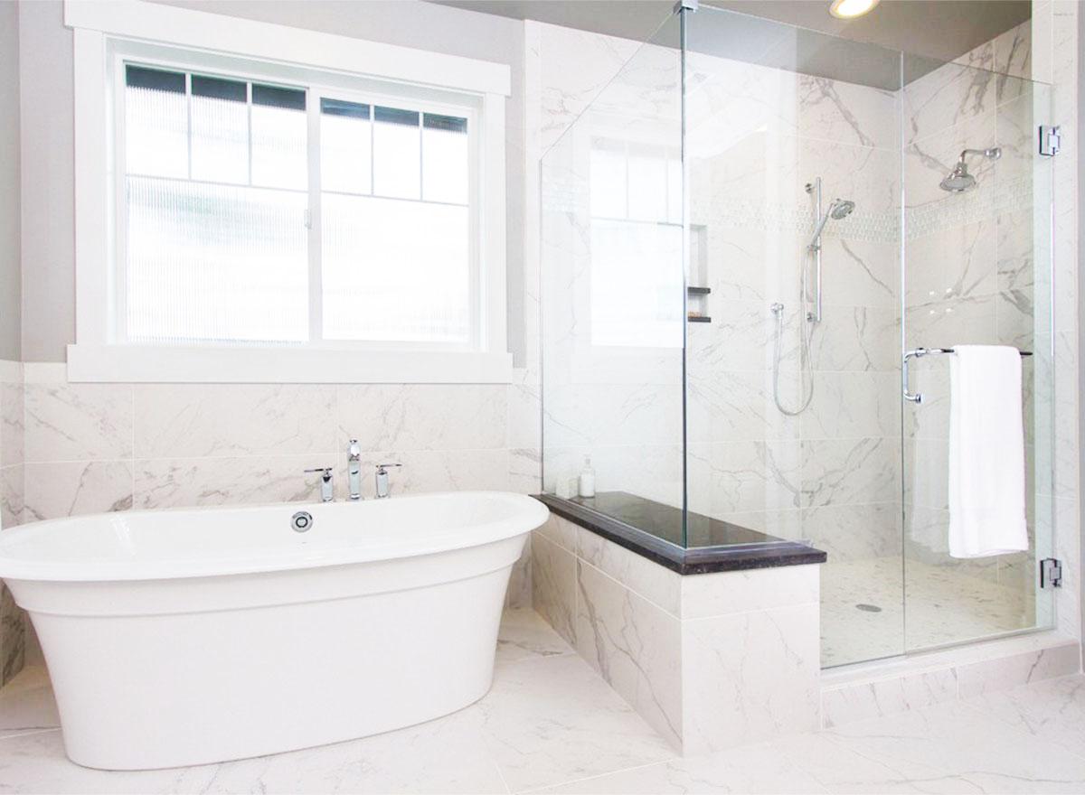 Bathroom with freestanding tub, marble tile, and glass-enclosed shower with bench.