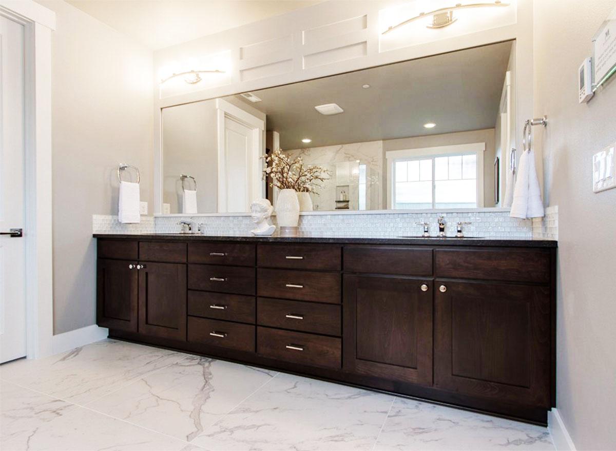 Bathroom vanity with double sinks, dark wood cabinetry, granite countertop, and large mirror reflecting a window.