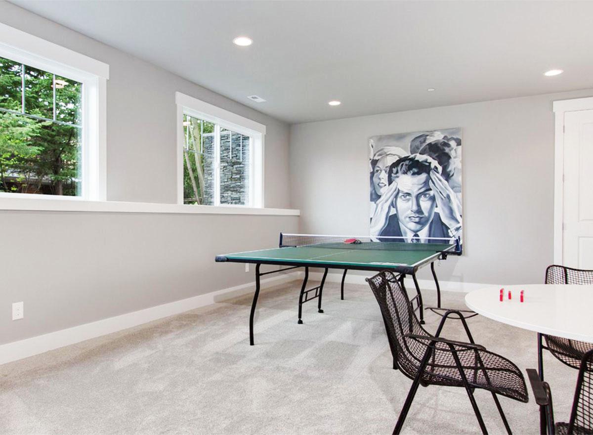 Interior view of a finished basement with a ping pong table, a small round table, and artwork on the wall.