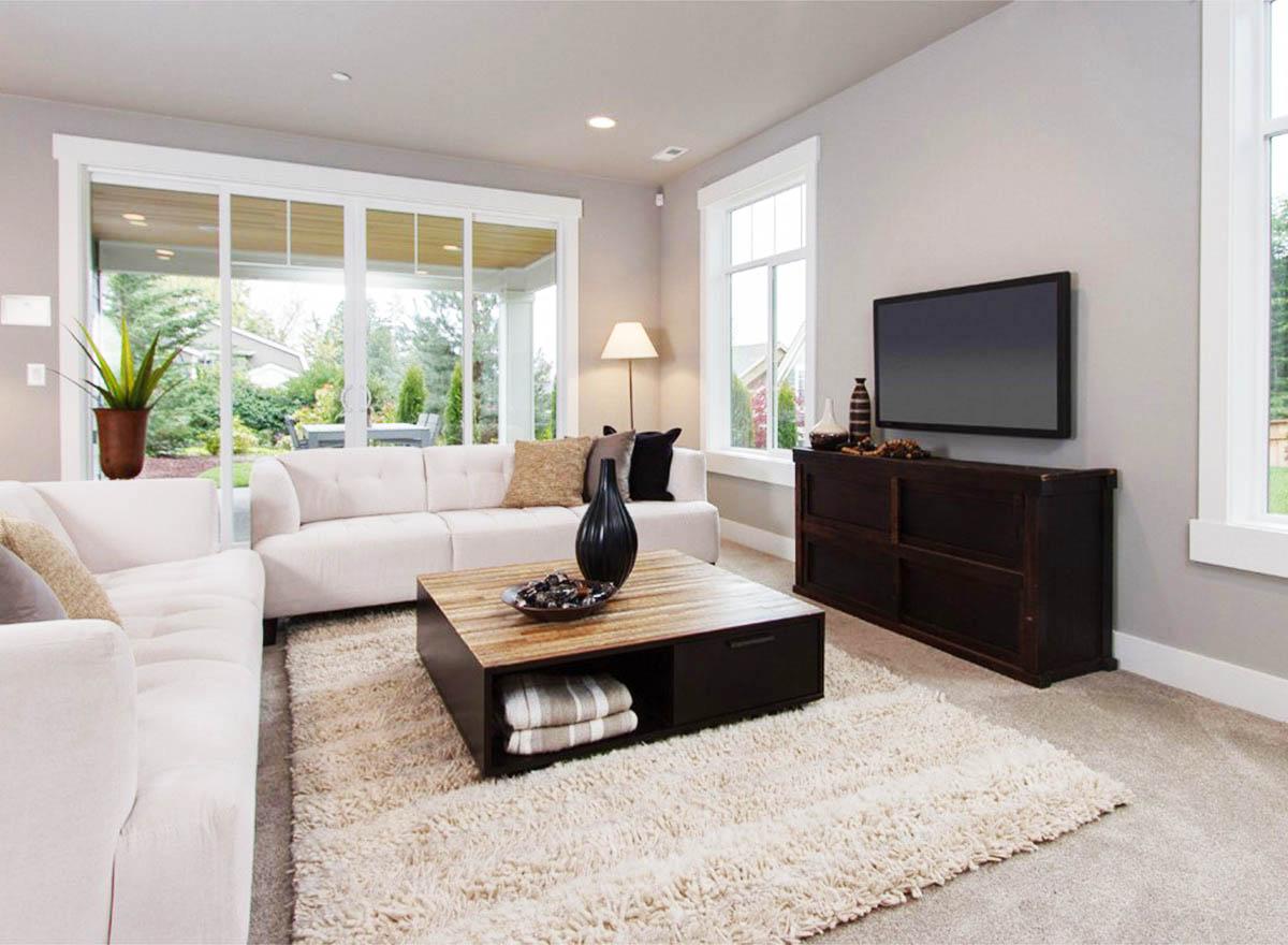 Living room interior with white sofas, wooden coffee table, large sliding glass doors, and a wall-mounted television.