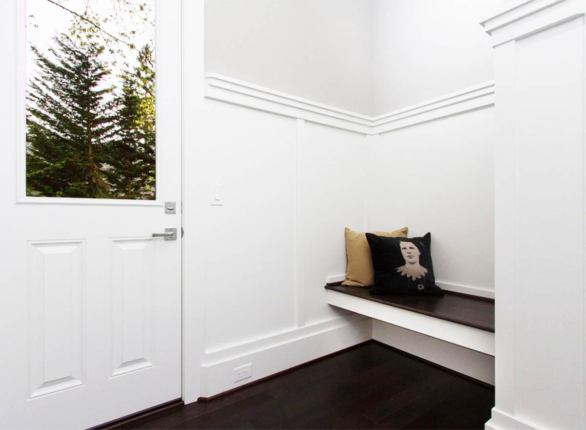 Mudroom with paneled door, built-in bench with pillows, and wainscoting.
