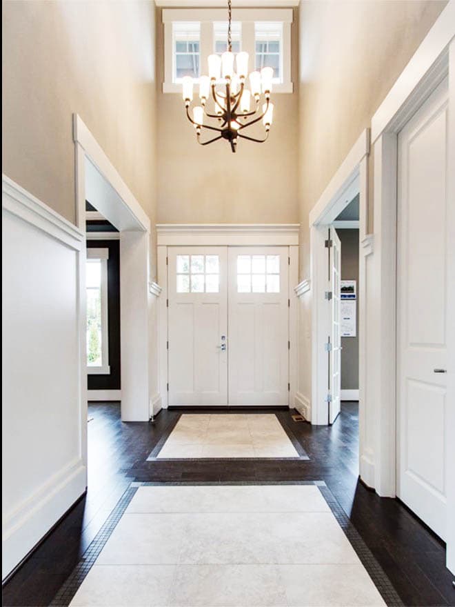 Interior view of a double-door entry with a tall, vaulted ceiling, chandelier, and inset tile flooring.
