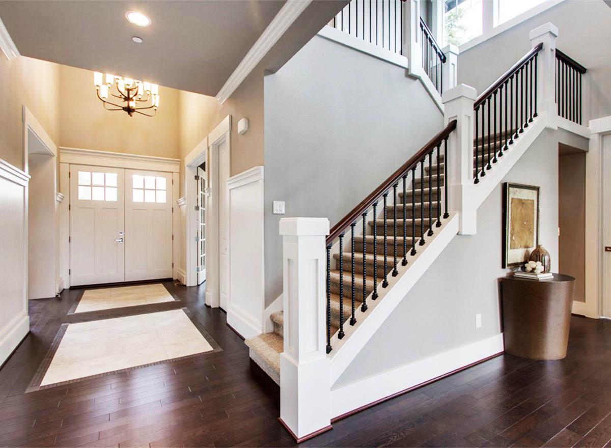 Interior view of a foyer with double doors, a grand staircase with wrought iron balusters, and dark hardwood floors.
