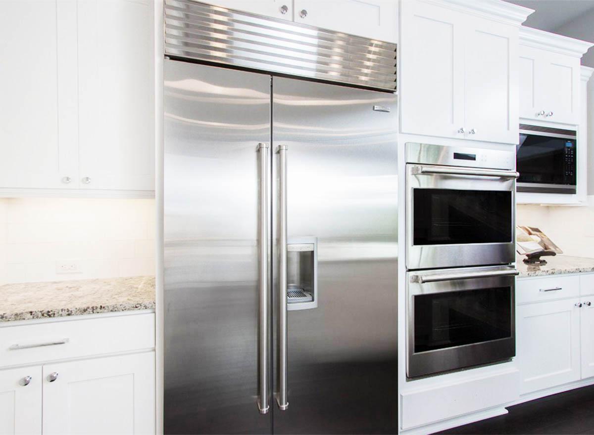 Kitchen featuring stainless steel side-by-side refrigerator, double oven, and microwave with white cabinetry.