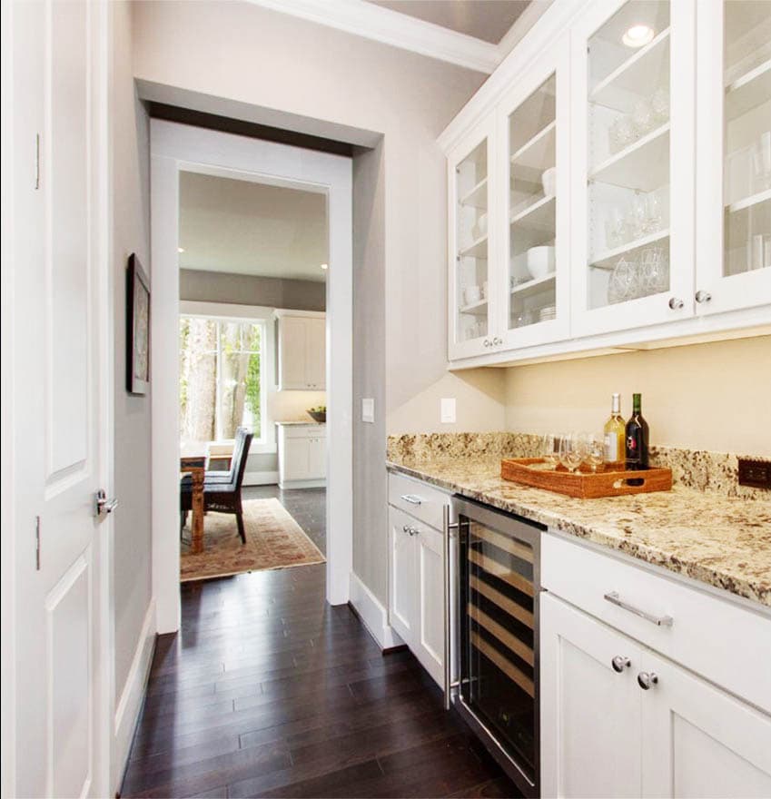 Butler's pantry with white cabinets, granite countertops, wine cooler, and view into dining area.