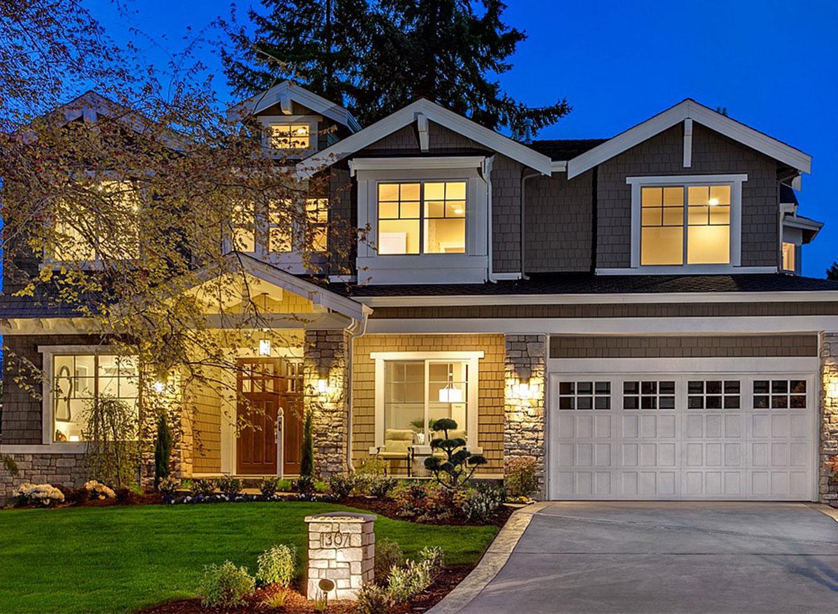 House plan exterior: two-story home with gabled dormers, covered entry, stone accents, and a multi-pane garage door.