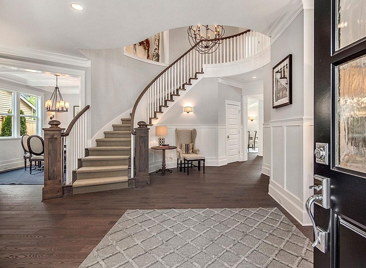 Foyer with curved staircase, wainscoting, hardwood floors, chandelier, and entry door.