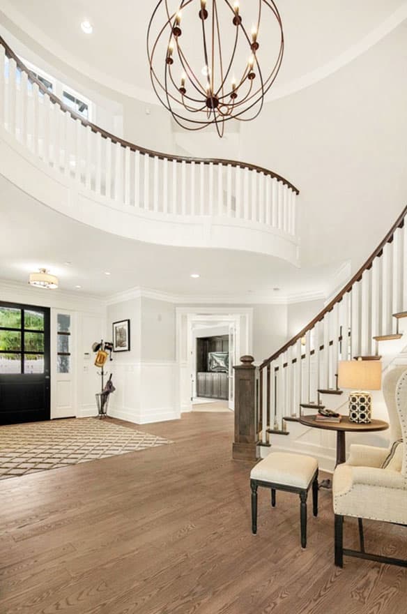 Interior view of a spacious foyer with a curved staircase, large chandelier, and entryway.