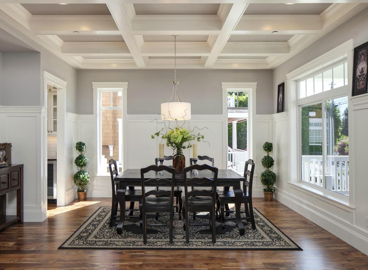Dining room with coffered ceiling, dark wood table and chairs, wainscoting, and large windows.