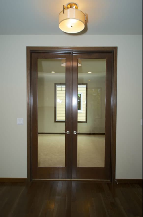 Double glass doors with dark wood frames open to a room with carpet and a large window.