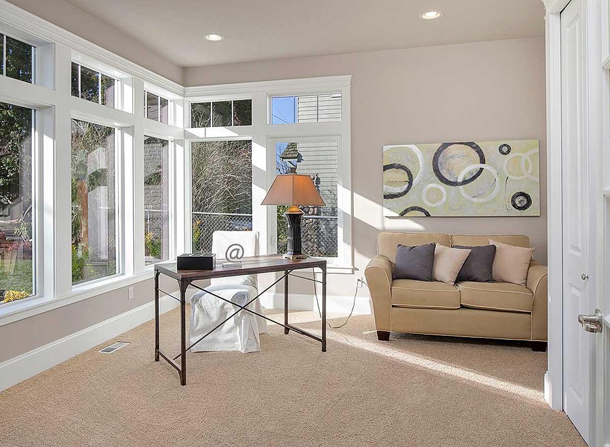 Interior view of a home office with a large bay window, desk, chair, and sofa.