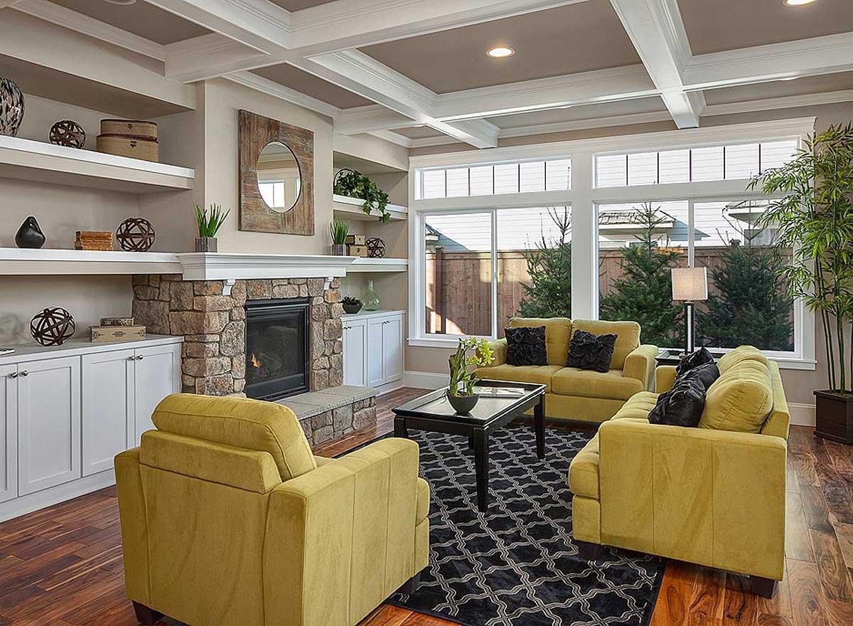 Living room with stone fireplace, built-in shelving, coffered ceiling, and large windows.