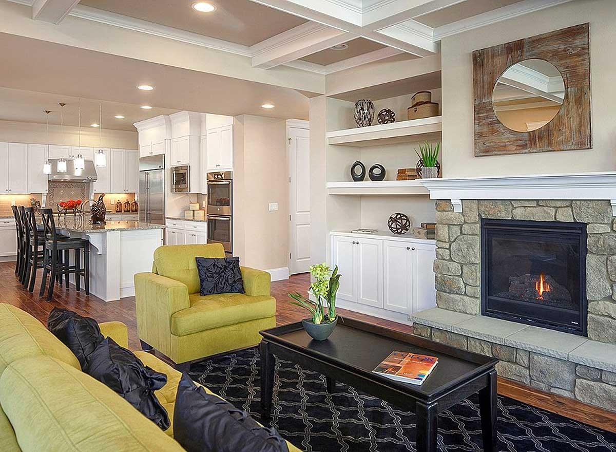 Interior view of a great room with kitchen, island, fireplace, built-in shelves, and coffered ceiling.