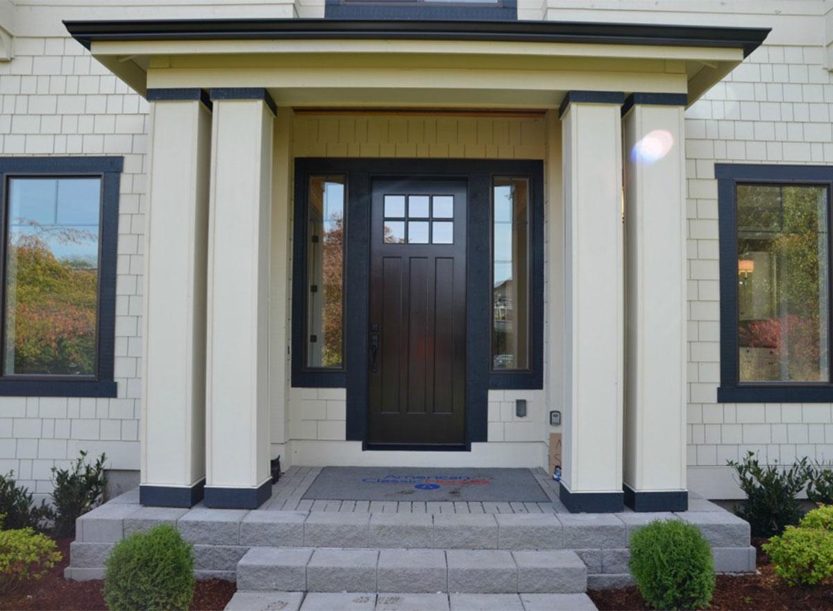 House plan exterior: Covered entryway with dual columns, shingled siding, and a dark wood door with sidelights.