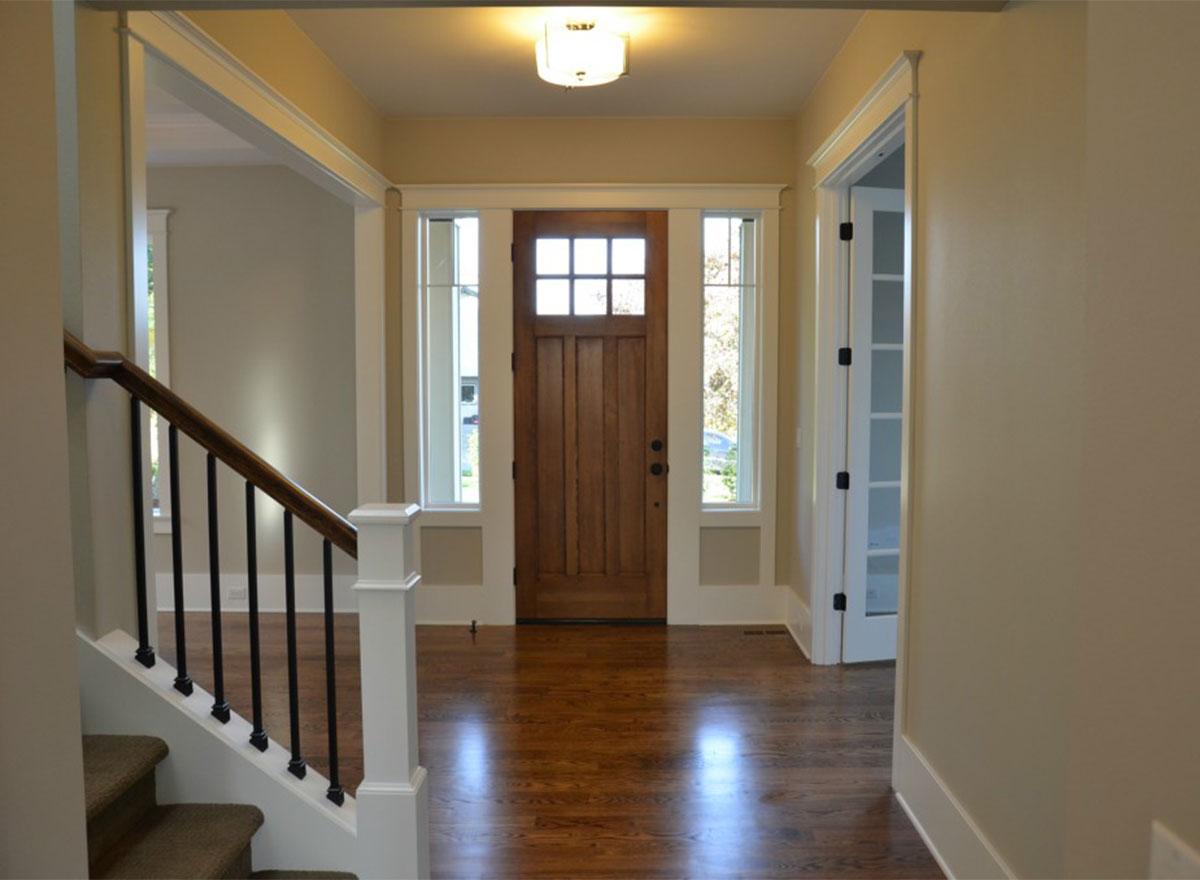 Interior view of house entryway with wooden door, sidelights, staircase, and hardwood floors.