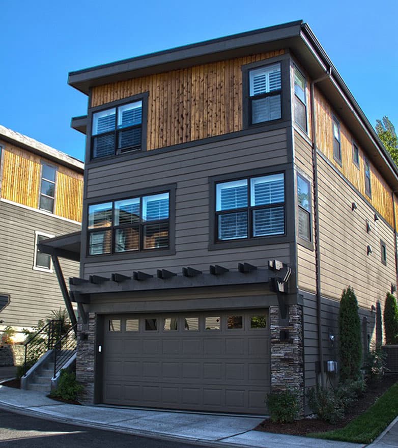 Modern house plan exterior with three stories, horizontal siding, wood accents, and attached garage with pergola.