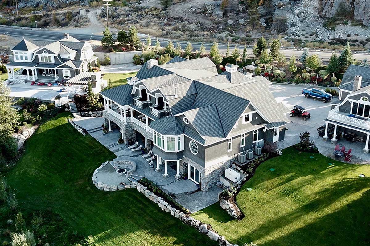 House plan exterior: Two-story gray home with gabled rooflines, wraparound porch, and stone foundation.