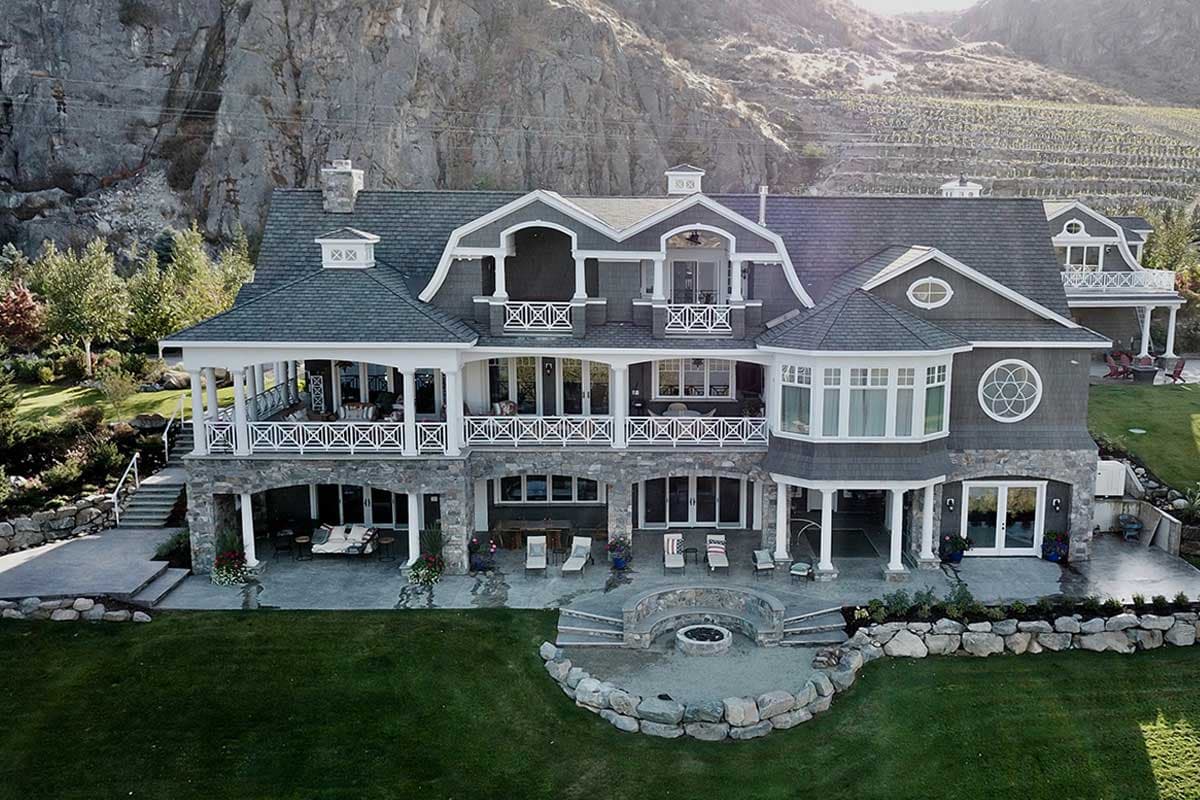 House plan exterior with stone base, multiple covered balconies, gambrel rooflines, dormers, and bay windows.