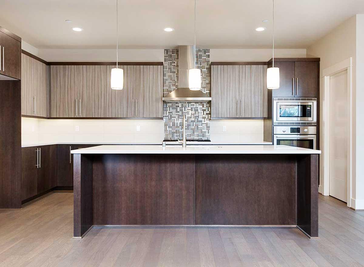 Modern kitchen with large island, two-tone cabinetry, stainless steel appliances, and mosaic tile backsplash.