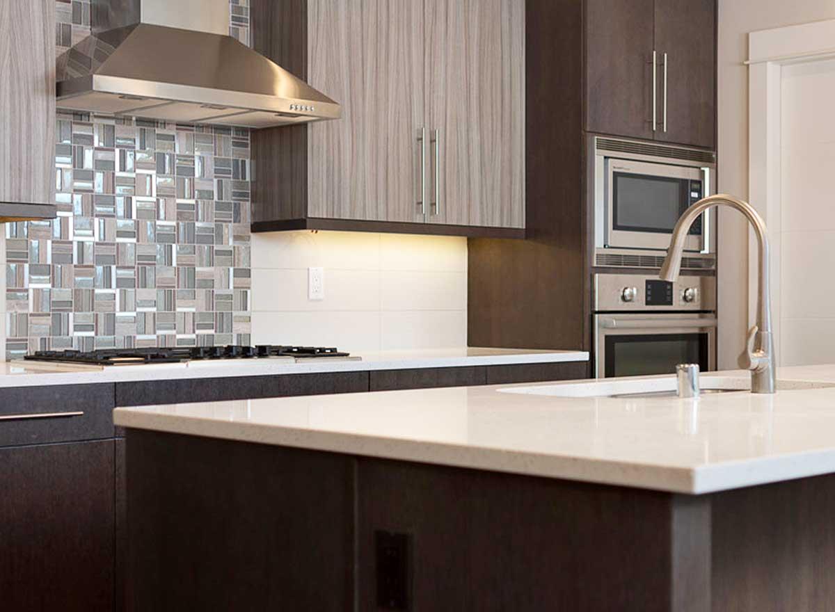 Modern kitchen with two-tone cabinets, mosaic tile backsplash, stainless steel appliances, and island.