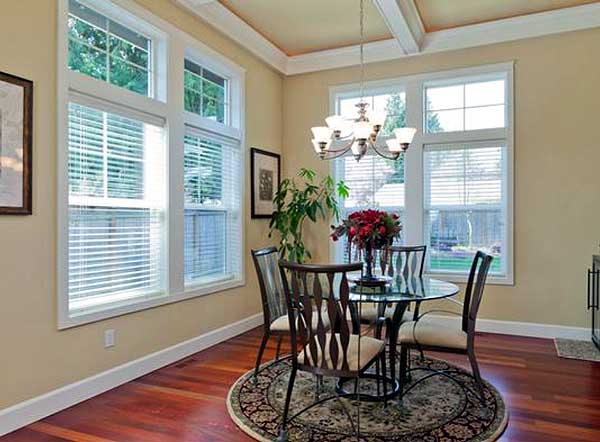 Dining room with glass table, chairs, coffered ceiling, and large multi-pane windows.