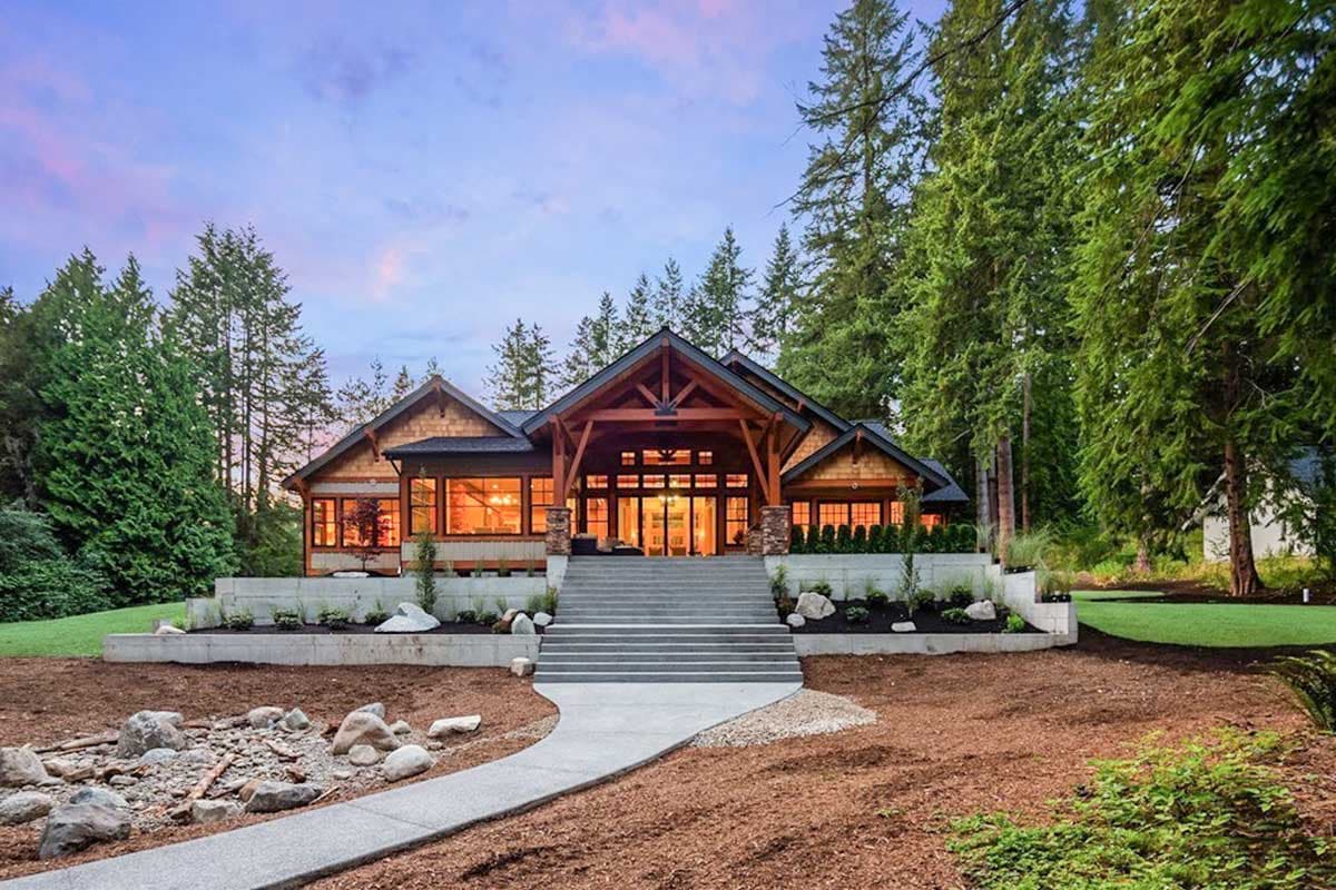 House plan exterior: Lodge-style home with large timber-framed entryway, extensive windows, shingle siding, and a wide tiered staircase.