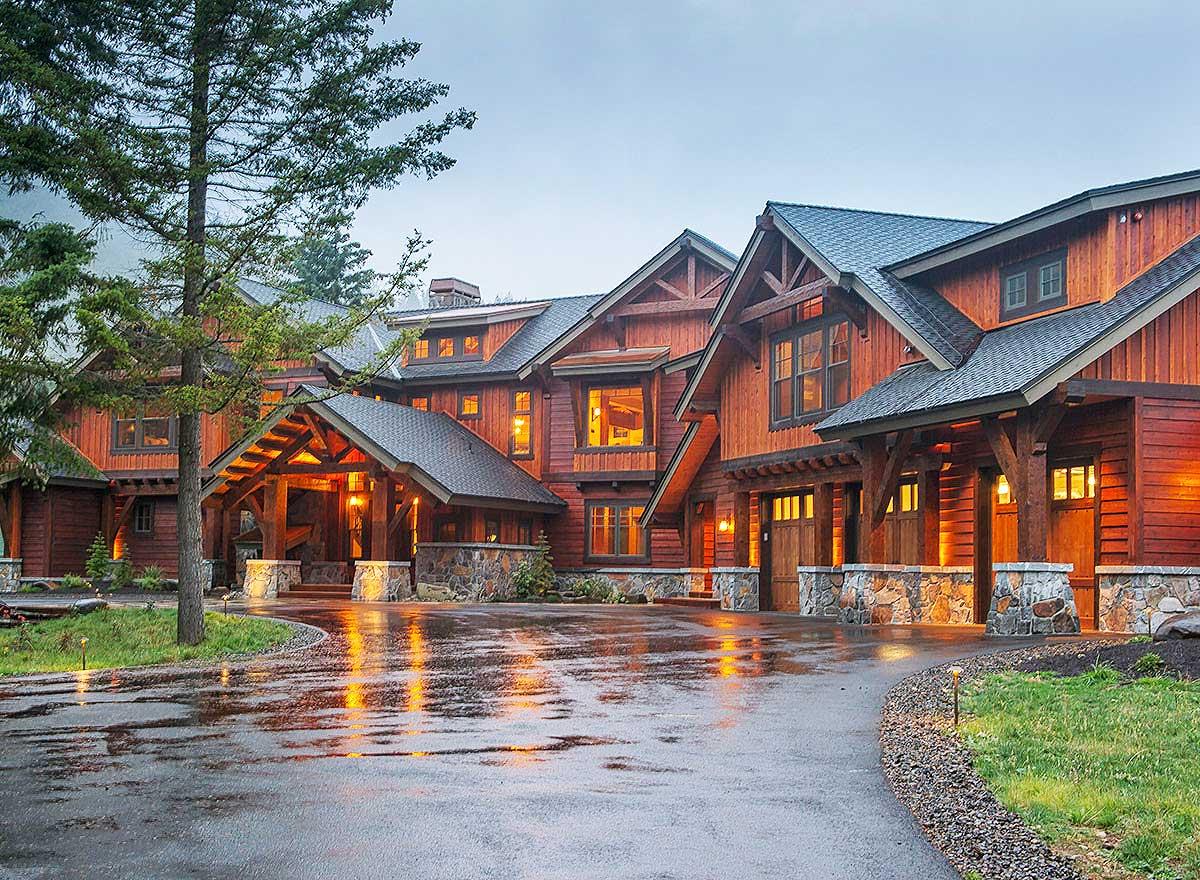 House plan exterior. Craftsman style with exposed timber framing, stone accents, multiple gables, and a porte-cochere. Two-story home with a garage.